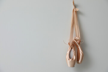 Beautiful beige ballet shoes with cute ribbons hanging on light grey wall. Space for text © New Africa