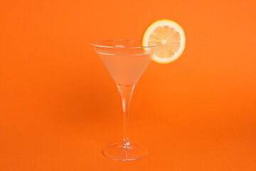 Martini glass of refreshing cocktail with lemon slice on orange background