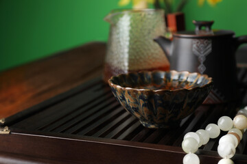 Cup with freshly brewed pu-erh tea and prayer beads on wooden tray, closeup. Space for text