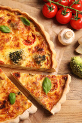 Delicious homemade vegetable quiche and ingredients on wooden table, flat lay