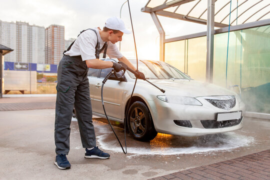 Young Guy In Uniform Car Wash Worker Washes Car With Water From Hose