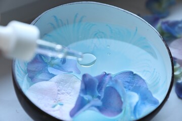 Fototapeta na wymiar Dripping essential oil from pipette into bowl with water and flowers, closeup