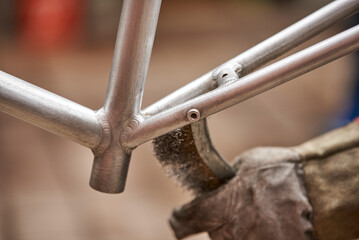 Unrecognizable man using a wire brush over a bicycle frame after passing a blowtorch over it to remove the paint, as part of his bike renovation work. Close up view.