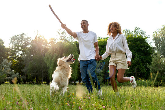 young african american couple play with dog in park on green grass and run