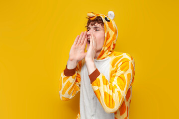 young joyful guy in funny children's giraffe pajamas announces and shouts to the side on yellow...