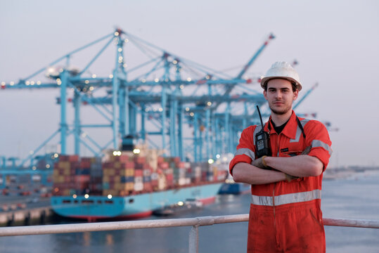 Offshore technician. Seafarer. Seaman. Navigator. A man in a boiler suit is standing in front of the port. Seafarer in front of the container terminal.