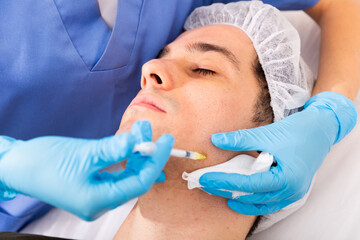 Young man caring of his skin, getting injection for face skin tightening at aesthetic clinic