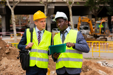 Two men workers working at the laying paving slabs facility discuss the project, holding important work documents