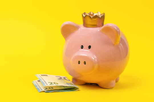 A pink piggy bank wearing a crown on a yellow background, with paper money. A whimsical and vibrant image representing savings and financial goals