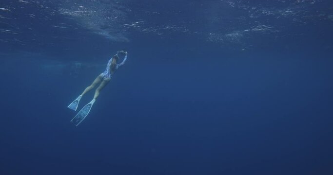 Underwater photographer. Man slowly swim underwater with professional camera housing in freshwater beautiful woman floats under water dark background, girl swims to surface of water, creating bubbles