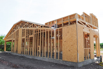 Partially framed single-family home under construction with wood studs, roof trusses, and OSB wall sheathing, representing early residential development phase on concrete foundation