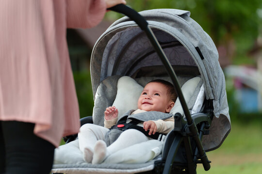 mother pushing happy infant baby stroller and walking in park