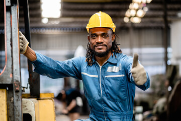 African American male worker smiling in safety uniform show thumb up in heavy metal manufacture...