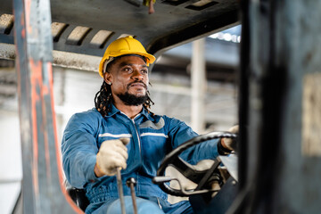 African American male worker in safety uniform driving forklift truck moving product in heavy metal...
