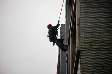 Window cleaning worker hanging on a building wearing safety equipement including harness and helmet.