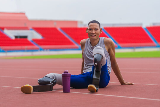 Happy Asian speed runner, with two prosthetic running blades, enjoys a restful moment on the stadium track after a rigorous speed running practice session