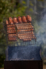 Cooking delicious and juicy sausages on the grill close-up. Roasted sausages on fire with smoke. Coocking hot food in nature on the weekend