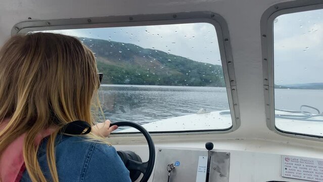 Woman with Blonde hair driving a small white motor boat on a lake. Over the shoulder shot.