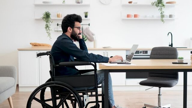 Close up view of smiling wheelchair user typing on portable computer while staying in distant workplace. Cheerful professional performing business project while doing full-time job from home.