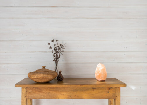 Oak side table with rustic accessories against white painted wood panelled wall including salt lamp, basket and dried seed pods (selective focus)