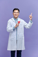 Handsome young doctor man holding paper with red heart, very happy pointing with hand and finger