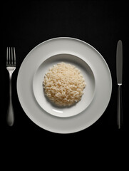 Rice on a plate with fork and knife on a black background.AI Generated
