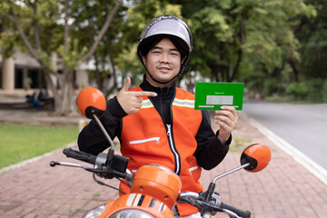 Happy young Thai motorcycle taxi driver or rider waiting for passenger near by the building in the...