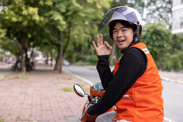 Happy young Thai motorcycle taxi driver or rider waiting for passenger near by the building in the...