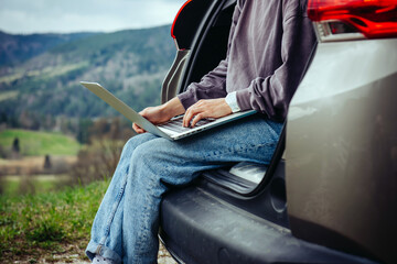 Downshifter woman sits in the trunk of a car and works on a laptop closeup during her journey...