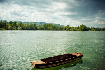 Naklejka na ściany i meble A small wooden fishing boat on the Drina River, in Serbia on a cloudy but sunny day. Reflection of sunlight in turquoise water
