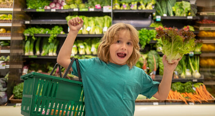 Child with lettuce salad. Child choosing fruits and vegetables during shopping at vegetable supermarket.