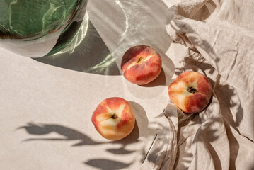 Ripe peaches on tan beige tabletop background with abstract aesthetic sunlight shadows, summer...