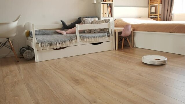 Robotic vacuum cleaner working on laminate wood floor in the living room. Automated white vacuum cleaner robot in the Scandinavian interior designed house