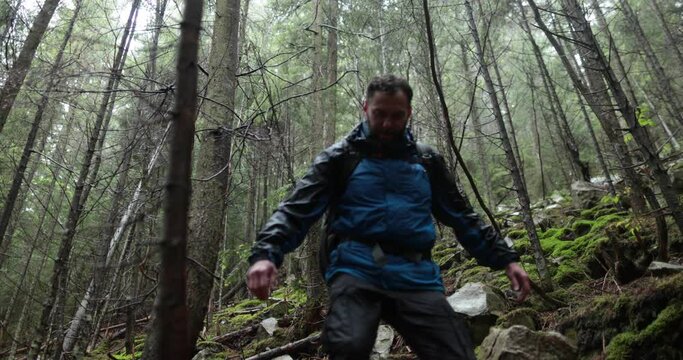 A young man in a mountain hiking with a backpack among the trees in a dense foggy forest. Single hike in long weather.