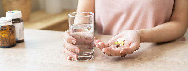 Sick, asian young woman, girl hand holding pill capsule, painkiller medicine from stomach pain, head ache, pain for treatment, take drug or vitamin and glass of water at home, pharmacy and health care - obrazy, fototapety, plakaty