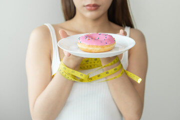 Diet, Dieting restrain asian young woman hand holding plate of donut, wrapped around arm with tape...