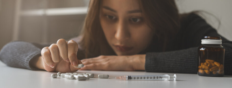 Anti drugs, drug addict asian young woman hand holding pills, medicament with narcotic syringe on table at home, abuse overdose. Sick pain of health, unhealthy people. Suicide depressed or despair.