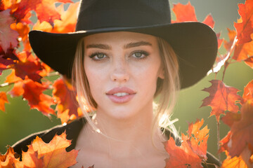 Close up portrait of a beautiful girl in black hat near colorful autumn fall leaves. Pretty tenderness autumn model.