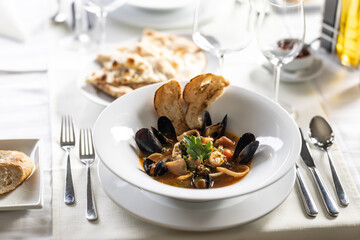 Seafood soup with mussels, fish, shrimp and other served with pastry on a nice table setting
