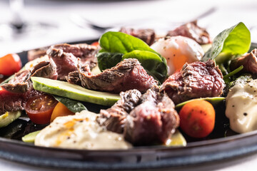 Paleo diet with flank beef steak, spinach leaves, avocado, tomatoes, eggs and basil leaves on a plate