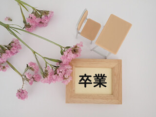 卒業の文字と学校の机とイス、ピンクの花