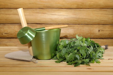 Fresh birch whisk, hat, metal bucket and ladle are on a wooden bench in the interior of a log...