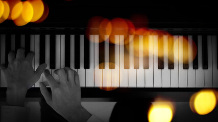 male musician hands playing on piano keys, black and white with golden light overlay.