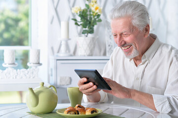 senior man using tablet while drinking tea