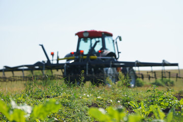 Red tractor with tooth harrow in the green field in Ukraine