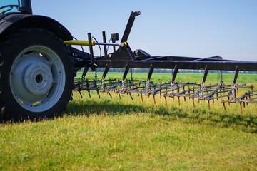 Red tractor with tooth harrow in the green field in Ukraine