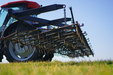 Red tractor with tooth harrow in the green field in Ukraine
