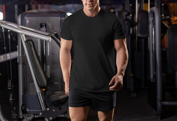 Fototapeta na wymiar Black t-shirt mockup on a walking muscular man in the gym, from head to knees, sportswear, front view.