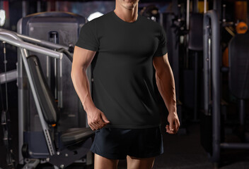 Fototapeta na wymiar Black t-shirt template on a posing athlete on the background of the gym, from head to knees, sportswear, front view.