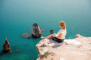 Freelance woman working on a laptop by the sea, typing away on the keyboard while enjoying the beautiful view, highlighting the idea of remote work.